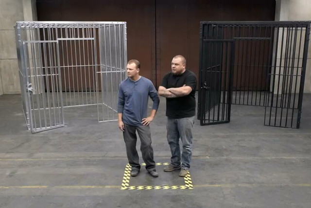 We first see a man or men standing in a large room in front of two cages. Screencap by author. 