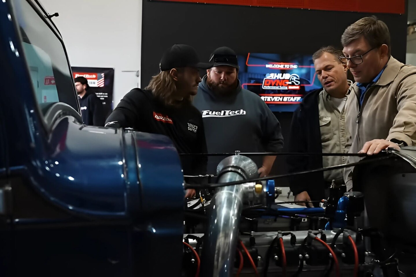four men looking at an engine of a car
