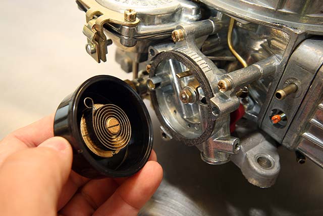 With the gasket on the choke housing, install the electric choke cap. Notice the metal tab sticking out from the housing. This must fit into the loop on the wound spring in the choke cap. You can check to make sure the tab is in the spring's loop by rotating the choke cap once it is in place. It should open and close the choke plate.