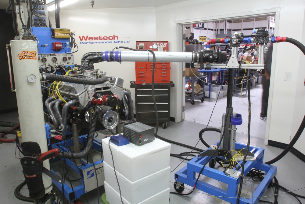 The compressed air cylinders are hidden behind the engine. The large tube feeds the compressed air. On the right are the series of valves that manage the compressed air as it enters the engine. The system can manage the pressure so it can be ramped up from 1-2 psi up to max pressure – all commanded by a simple laptop program. The gray device sitting on the white boxes is the 12-volt power supply for the ECU (blue box). The power supply will not be needed when installed in a car.